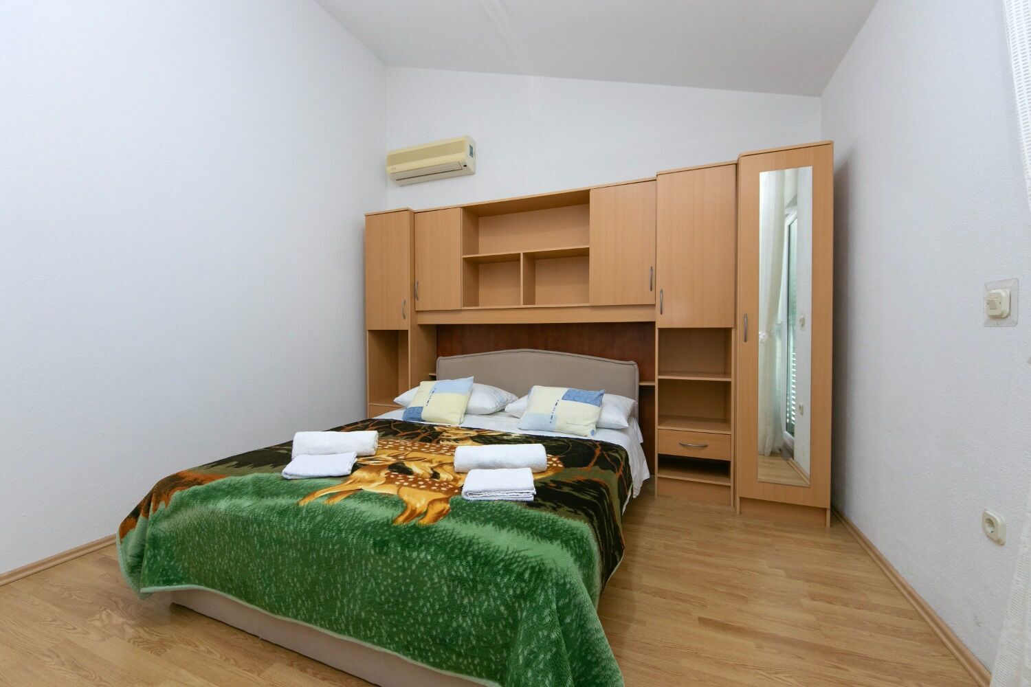 Ein Schlafzimmer mit einem Bett, einer grünen Decke, einem Spiegel und Holzmöbeln.