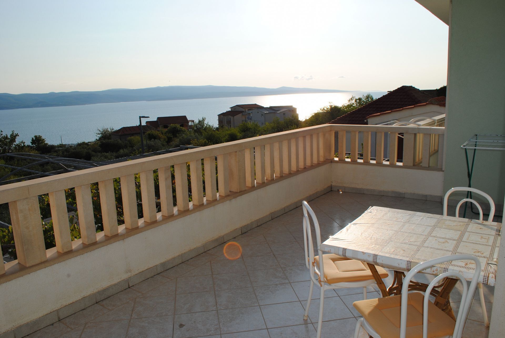 A balcony with a table and chairs, overlooking a body of water and distant hills.