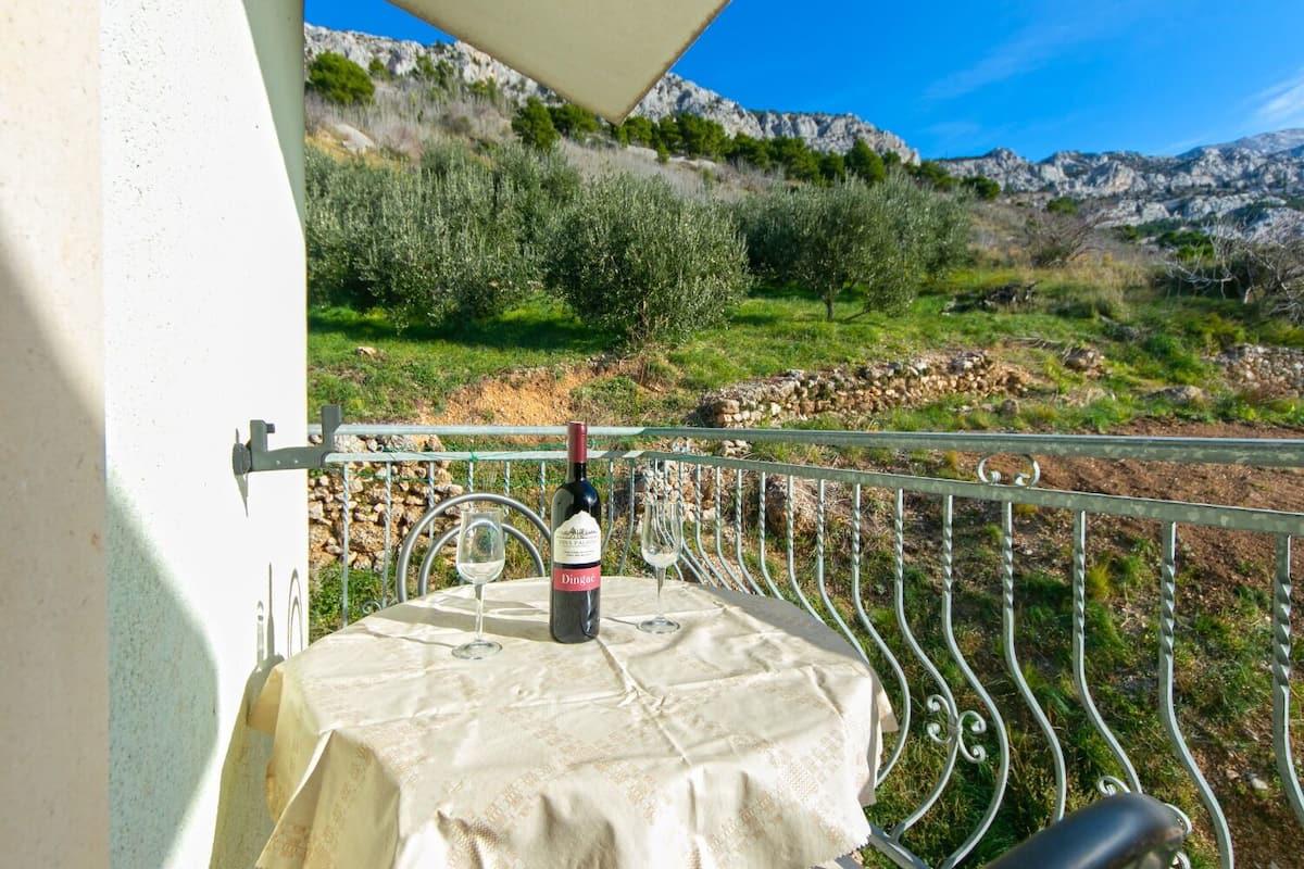 A balcony with a table set for two, a bottle of wine, and a view of a mountainous landscape.