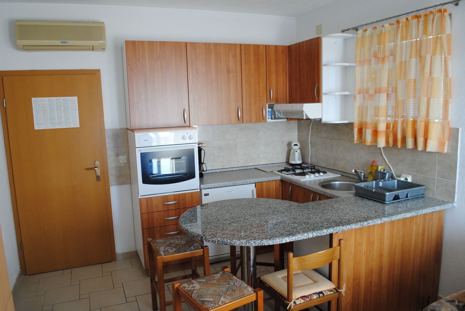 A compact kitchen with wooden cabinets, a built-in oven, a microwave, a gas stove, a sink, and a small dining area with two chairs.