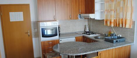 A compact kitchen with wooden cabinets, a built-in oven, a microwave, a gas stove, a sink, and a small dining area with two chairs.