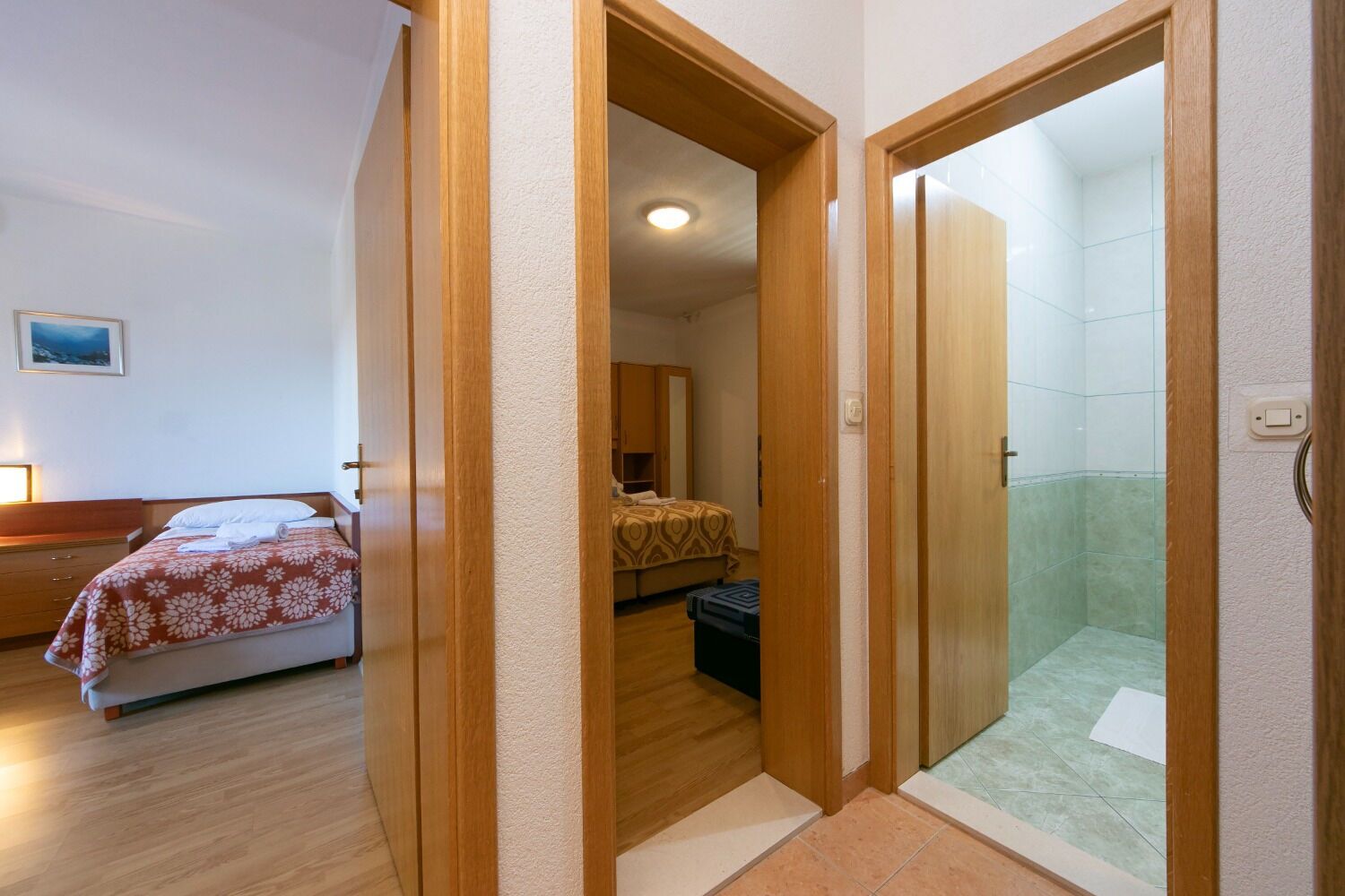 Ein Hotelzimmer mit Bett, einem Badezimmer mit Dusche und einem Gang, der zu einem weiteren Zimmer führt.