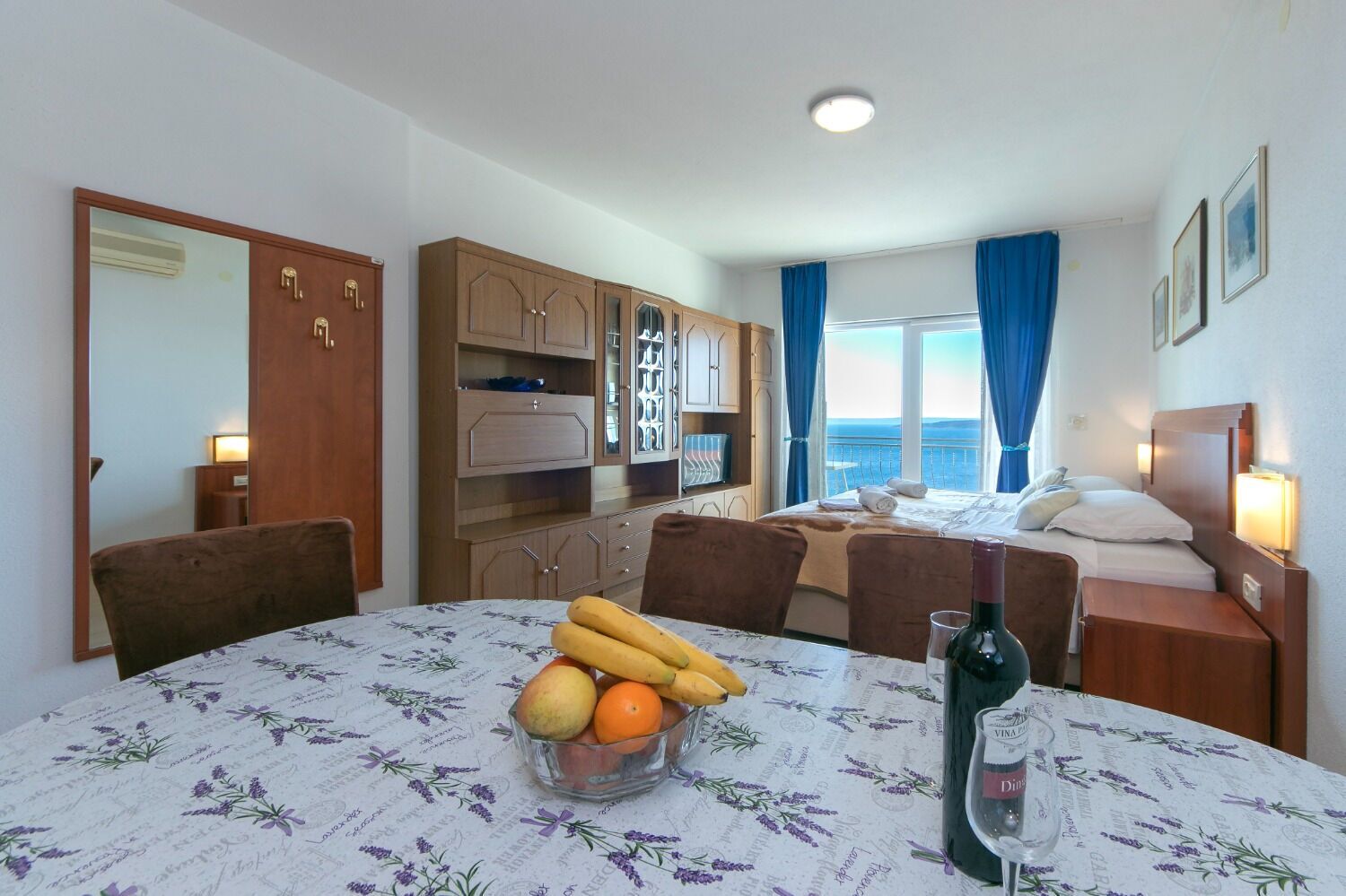 A hotel room with a dining area, a bed with a view, and a minibar.
