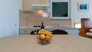 A kitchen with a dining table set with fruit and wine glasses, a stove, and a window above the sink. - Apartments Marko (Brela)