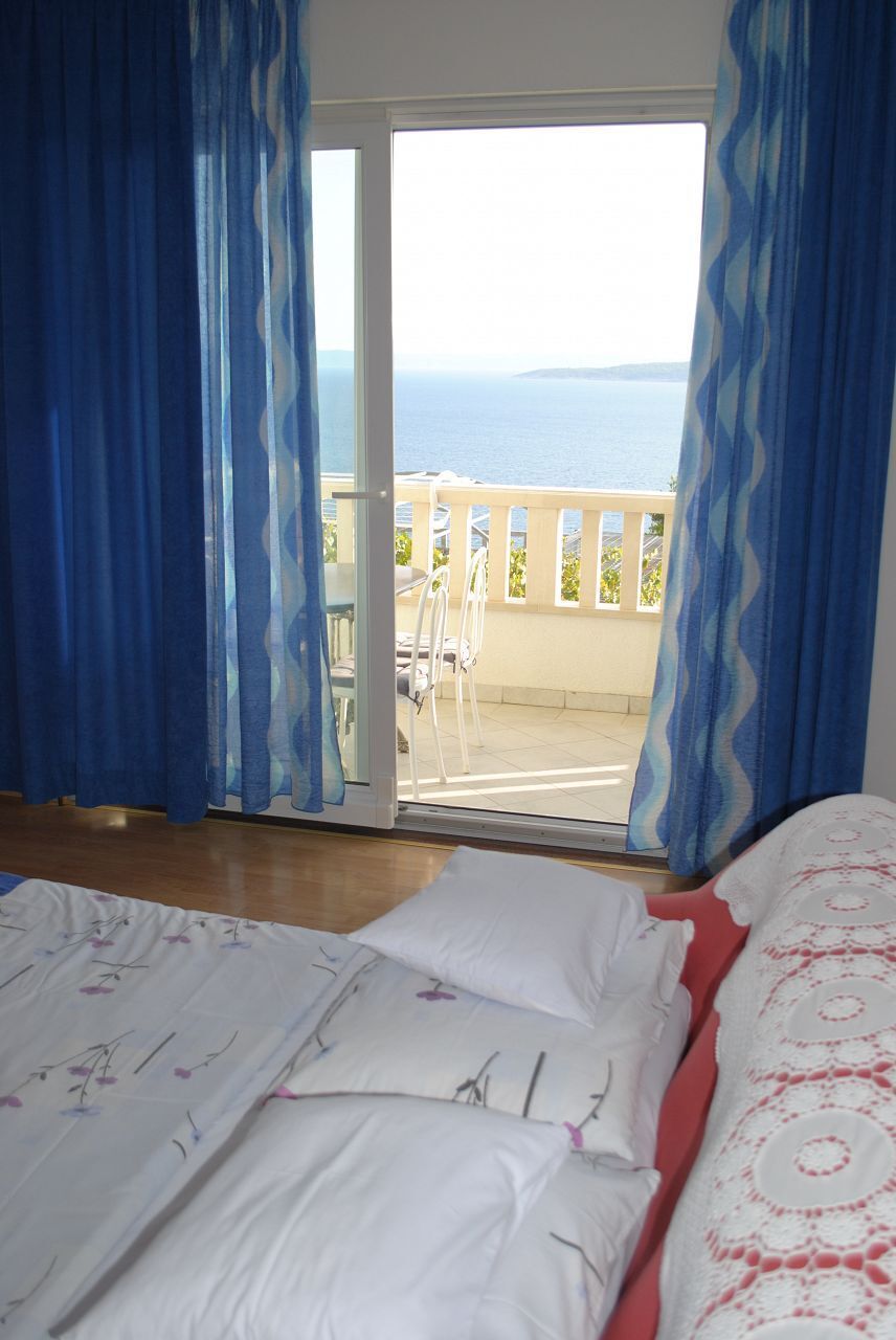 A bedroom with a bed, white bedding, and a view of the sea through a sliding glass door.