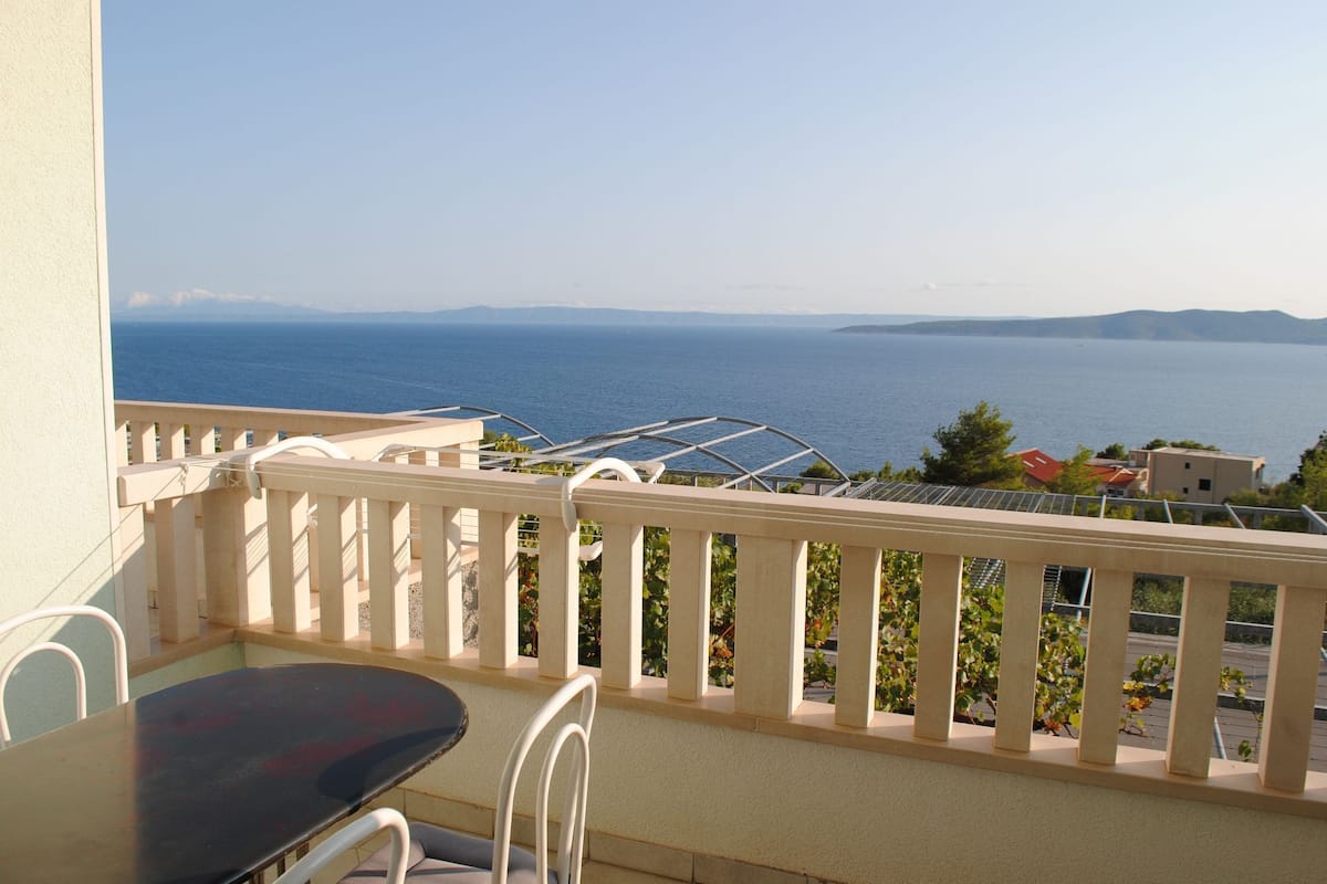 A balcony with a table and chairs, overlooking a body of water and distant land.