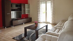 Una sala de estar moderna con un sofá, una mesa de centro con un florero, un televisor en un mueble y un ventanal corredero.