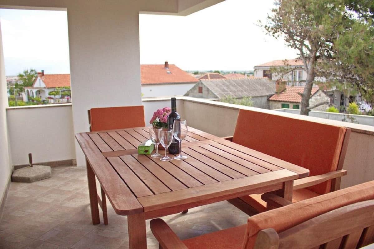 A wooden table with four chairs on a balcony, a bottle of wine, and a vase of flowers.
