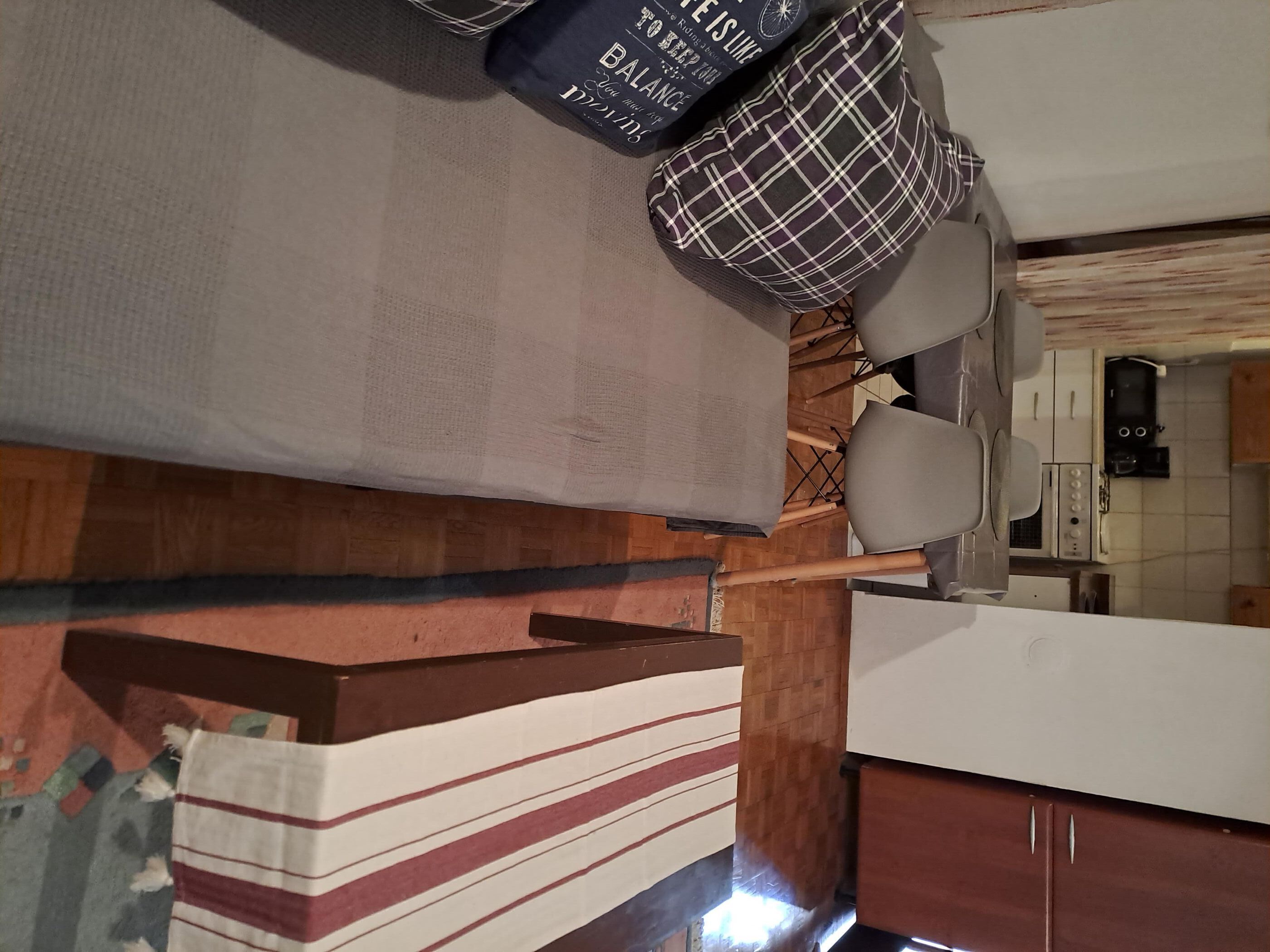 Una habitación con cama, mesita de noche, una silla y una cocina con armarios y estufa.