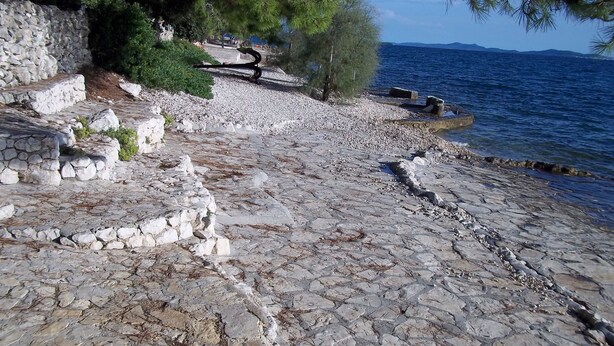 A stone pathway leading to a body of water, surrounded by trees and a stone wall. - Apartment Branka (Zadar)