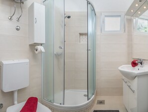A modern bathroom with a glass-enclosed shower, a toilet, and a sink with a red towel. - Apartments Milica (Dugi Rat)