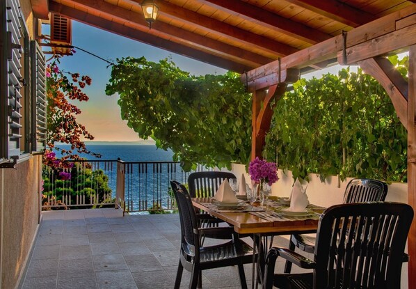 An outdoor dining area with a view of the sea, wooden pergola, and potted plants. - Apartments Milica (Dugi Rat)