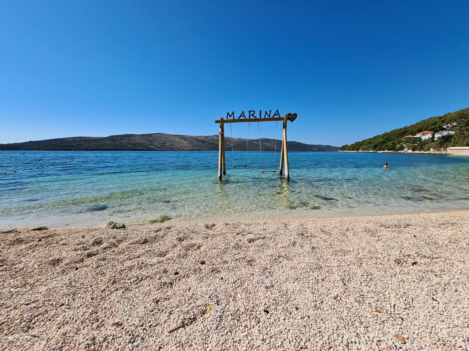 A pebble beach with a wooden swing set labeled "MARINA" in the water.