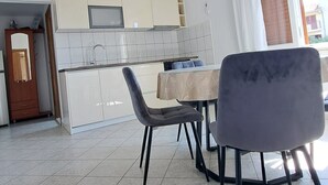 A spacious living area with a dining table and chairs, a kitchen with white cabinets, and a large window with curtains. - Apartments Ante (Seget)