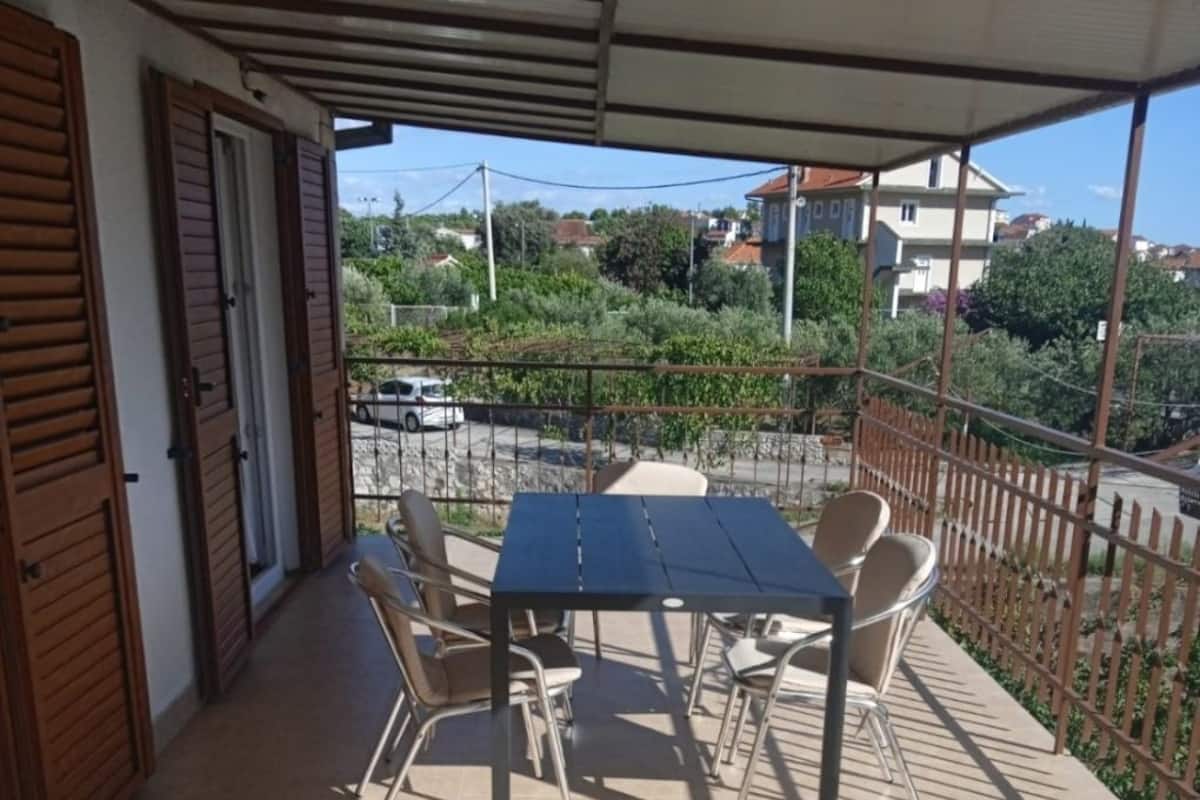 Une terrasse extérieure couverte, dotée d’une table et de chaises, d’un sol carrelé et offrant une vue sur le quartier environnant.
