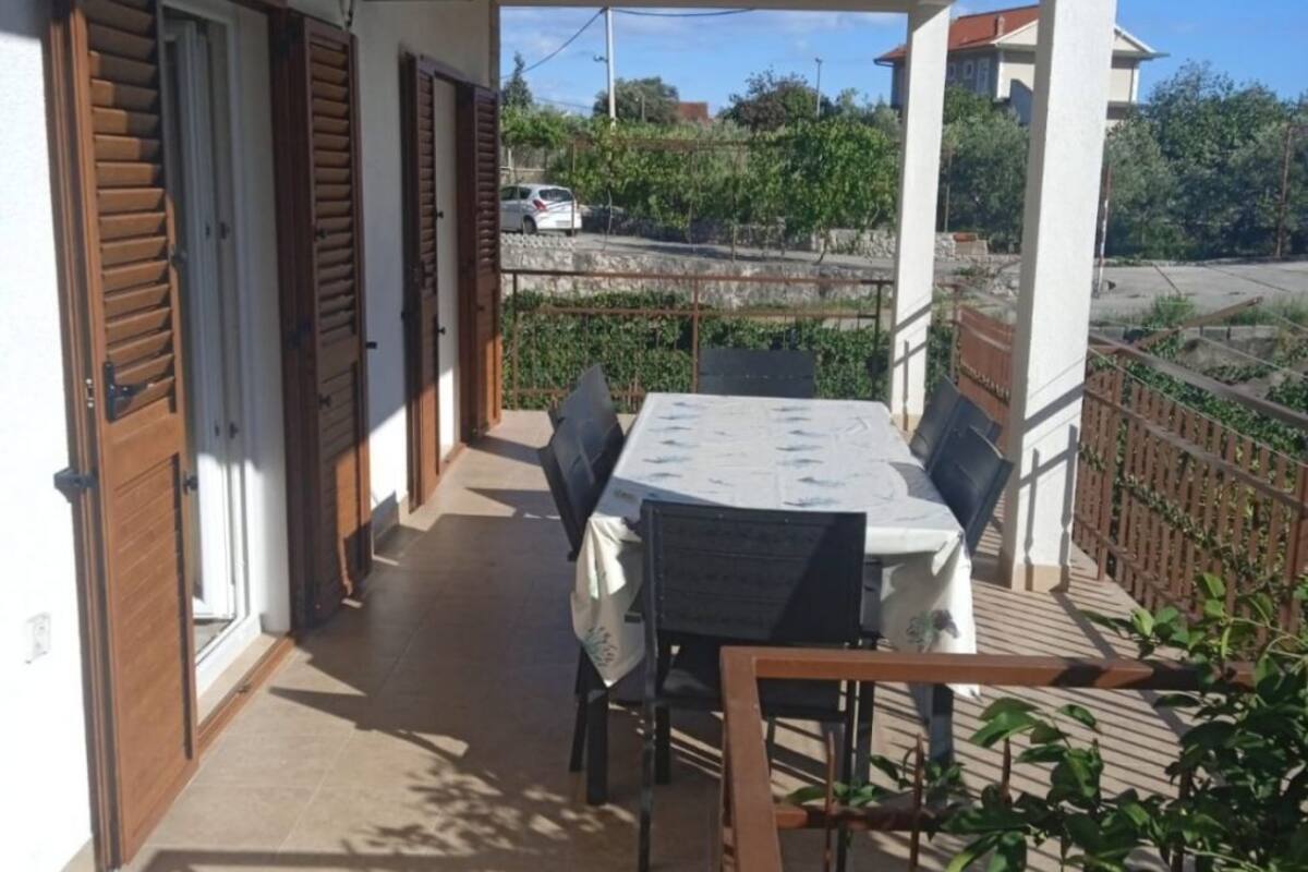 Un balcon avec une table et des chaises, un appareil de climatisation et une vue sur une rue et des espaces verts.
