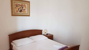 A neatly made bed with white linens and a purple towel, a wooden headboard, a bedside lamp, and a framed artwork on the wall. - Apartment Jakov (Nin)