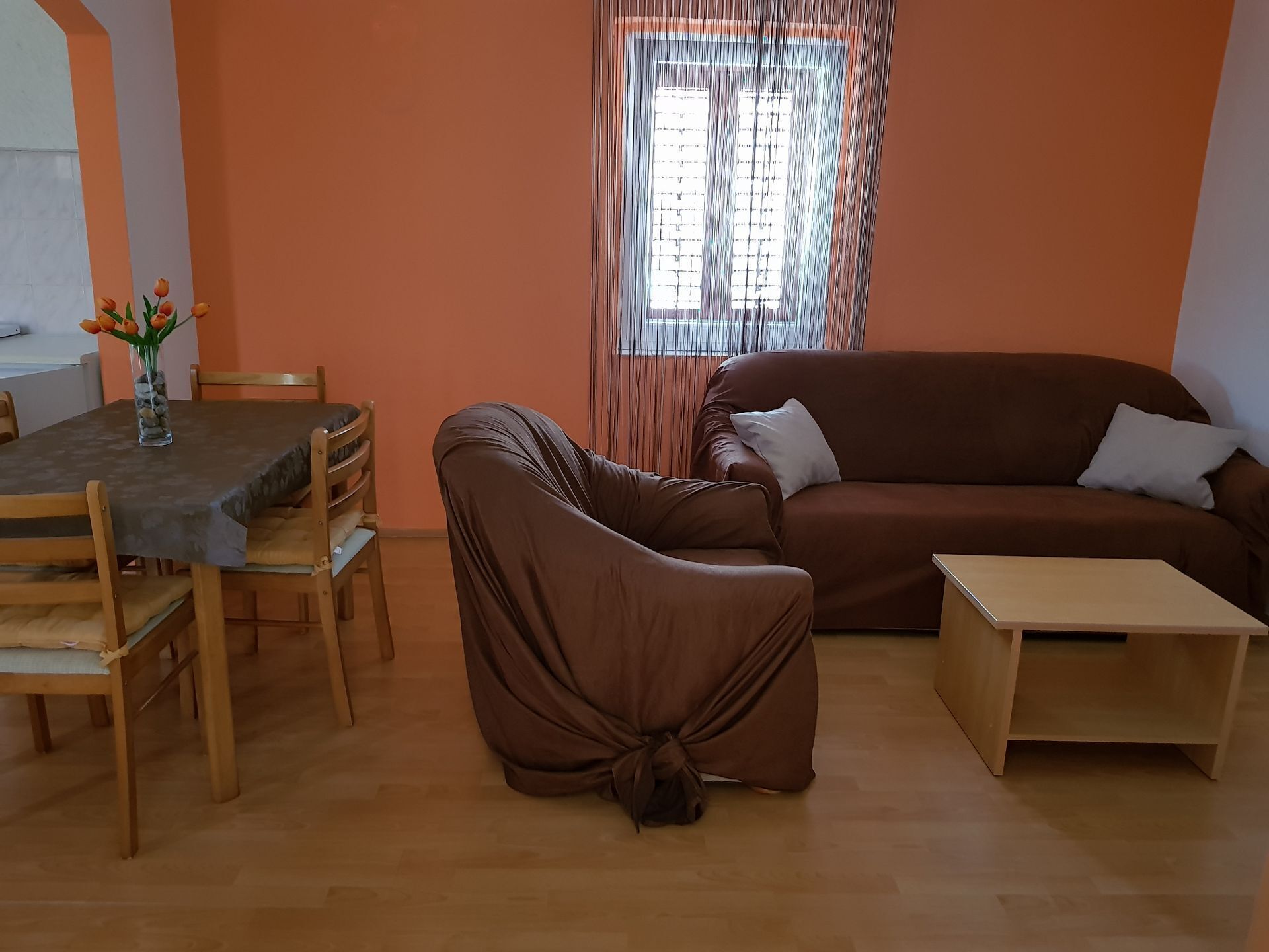 A living room with a brown sofa, a wooden coffee table, and a dining table with chairs.