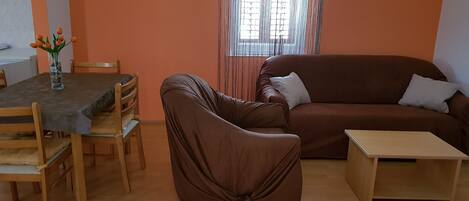 A living room with a brown sofa, a wooden coffee table, and a dining table with chairs.