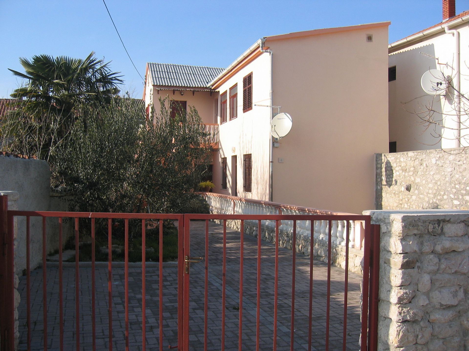 A residential area with a paved driveway, a red metal gate, and a stone wall.