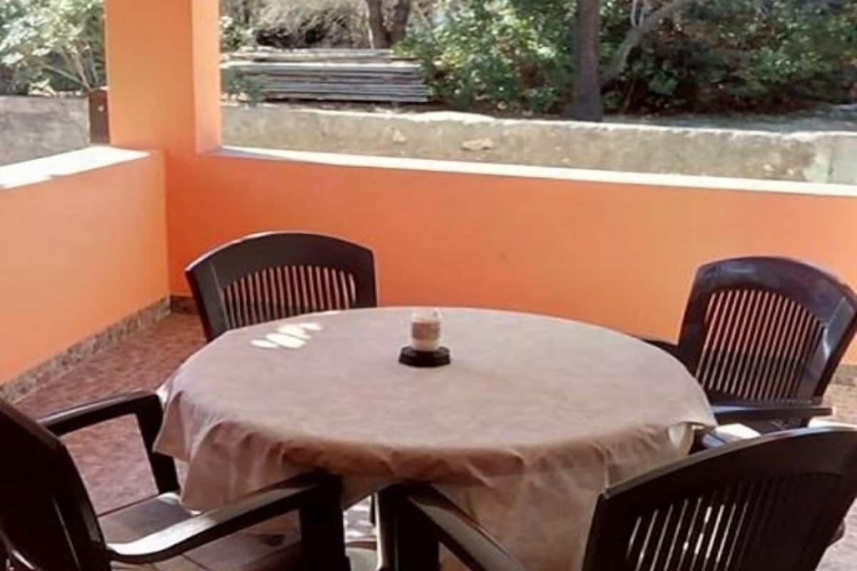 Un espacio de estar al aire libre techado con una mesa redonda y cuatro sillas, rodeado de paredes anaranjadas y vistas a árboles.