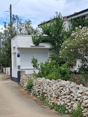 Ein weißes Gebäude mit einer Garage, umgeben von Grünflächen und einer Steinmauer.