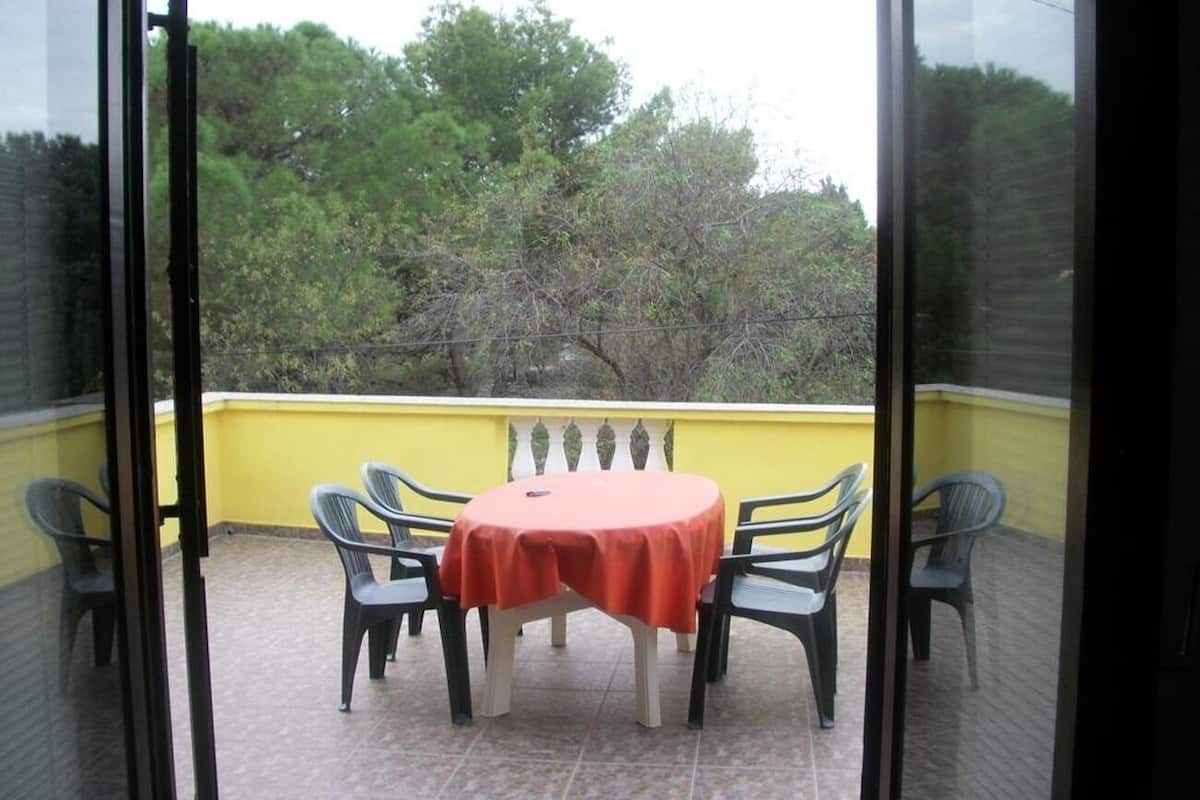 Un balcón con una mesa redonda y seis sillas, una pared amarilla y vistas a árboles.