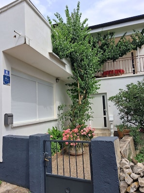 Un immeuble rĂ©sidentiel dotĂ© dâune entrĂ©e sĂ©curisĂ©e par un portail, dâun balcon avec une rambarde rouge et dâun petit jardin agrĂ©mentĂ© de fleurs roses.