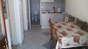 Una cocina pequeña y funcional con armarios blancos, un lavabo y una mesa de comedor con mantel floreado.