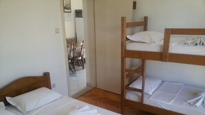 Una habitación con dos camas individuales, una litera, muebles de madera y una puerta que da a un pasillo con sillas.