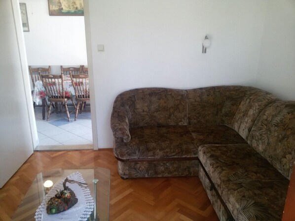 A living room with a patterned sofa, a glass table with a decorative item, and a dining area with chairs and a table in the background. - Apartment Mare (Pakostane)