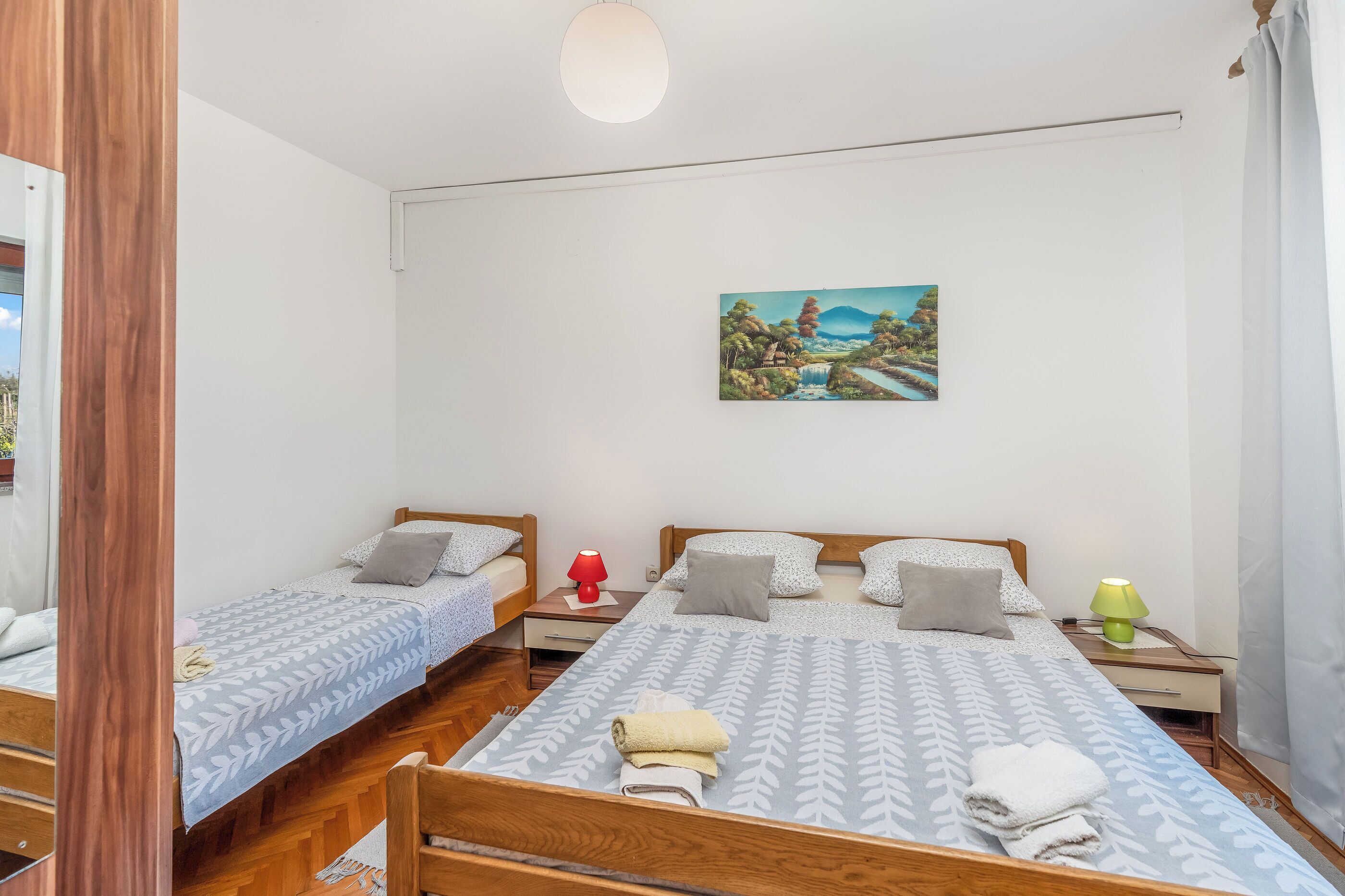 A bedroom with two single beds, a shared bed, a painting on the wall, and a nightstand with a lamp.