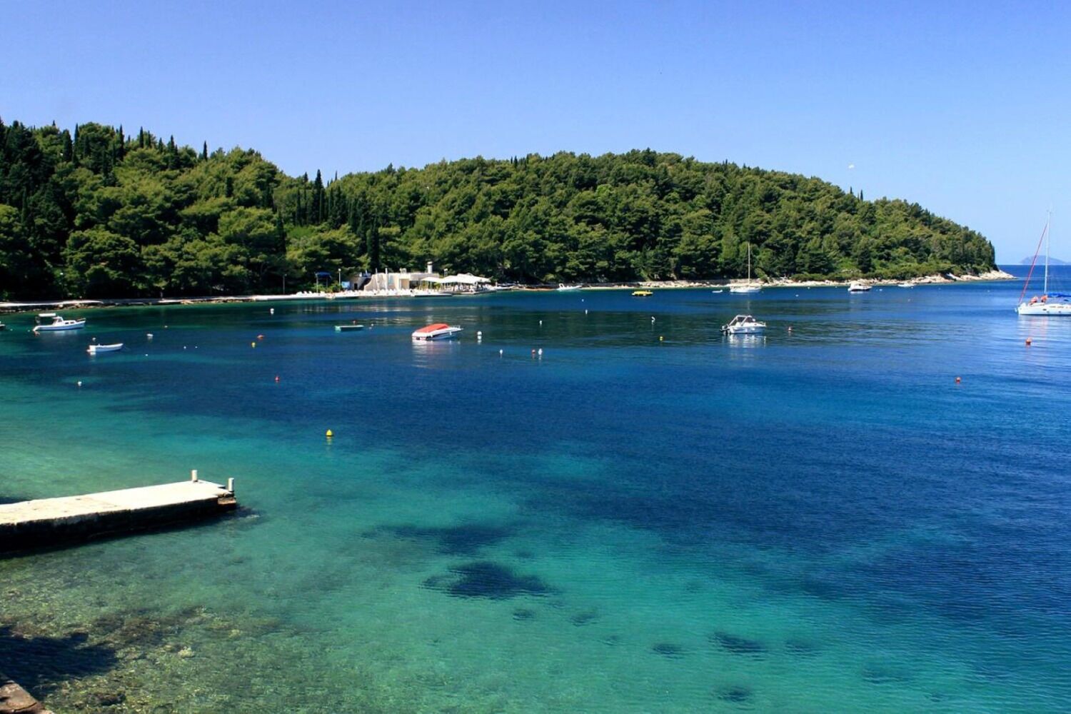 Eine Küstenlandschaft mit klarem türkisblauem Wasser, Booten und einem Steg.