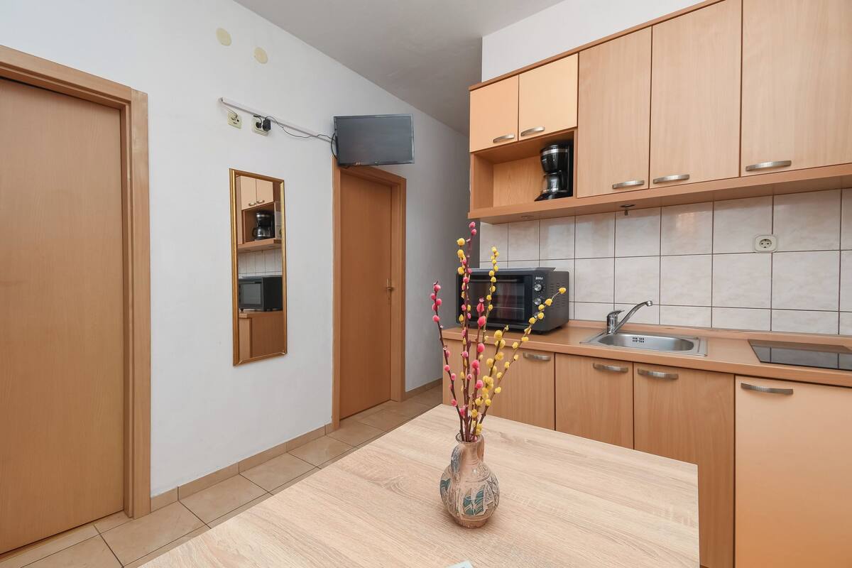 A modern kitchen with wooden cabinets, a built-in microwave, and a vase with flowers on the counter.