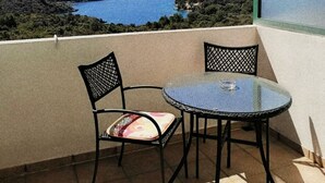 Ein Balkon mit rundem Glastisch und zwei Stühlen, mit Blick auf eine Küstenlandschaft, die einen klaren Meer- und Hügelblick bietet.