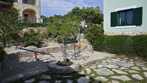 Ein gepflasterter Weg führt zu einem Spielplatz mit Schaukeln und einer Wippe.