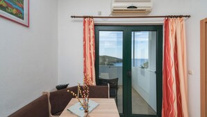 Ein Zimmer mit Esstisch, Stühlen, einer Vase mit Zweigen, einer Klimaanlage und Blick auf einen Balkon mit einer Tür.
