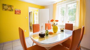 Un coin repas avec une table en verre, des chaises orange et un mur jaune.