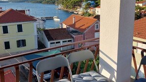 A balcony with two chairs and a table, overlooking a coastal town with buildings and boats. - Apartment Silvana (Sali)