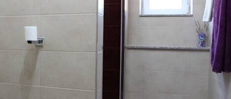 Un baño con un dispensador de papel higiénico, una ventana y una repisa con una toalla morada.