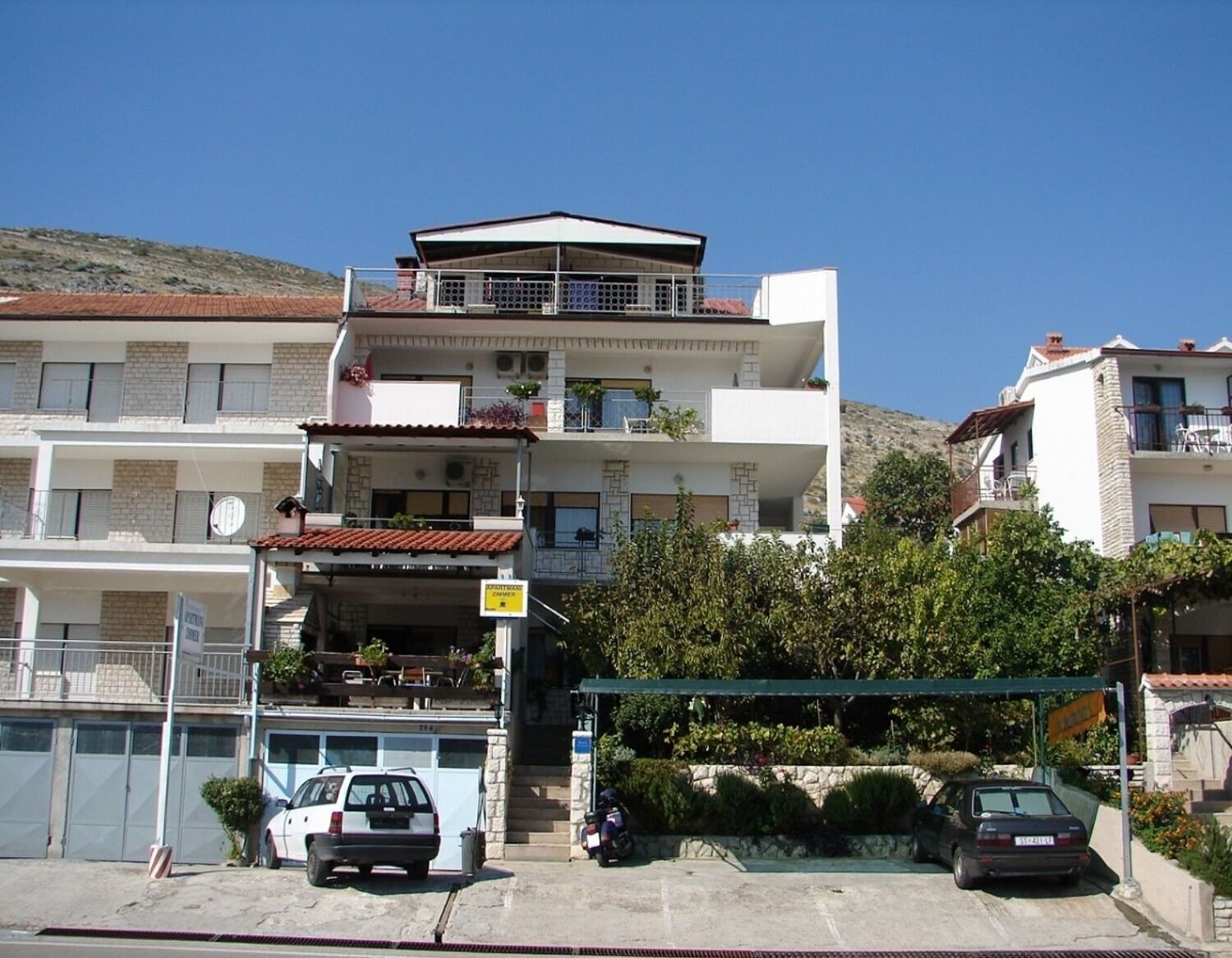Un edificio residencial de varios pisos con balcones, un garaje y un coche estacionado en frente.
