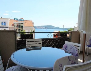 Ein Balkon mit Tisch und Stühlen, der auf ein Gewässer und ein fernes Gebirge blickt.
