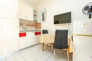 A compact kitchen with a dining area, a TV mounted on the wall, and a refrigerator. - Apartments Vesna (Sali)