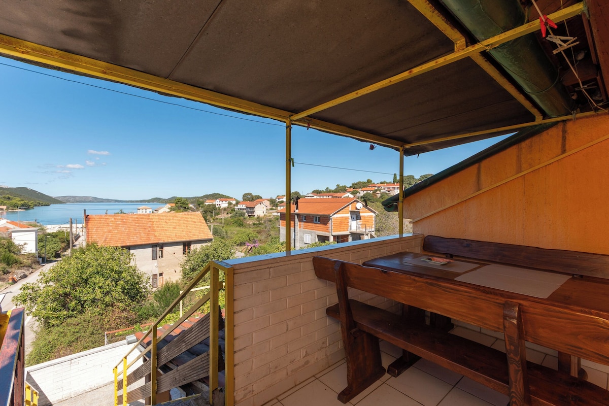 A balcony with a view of a coastal town, a wooden bench, and a staircase leading down.
