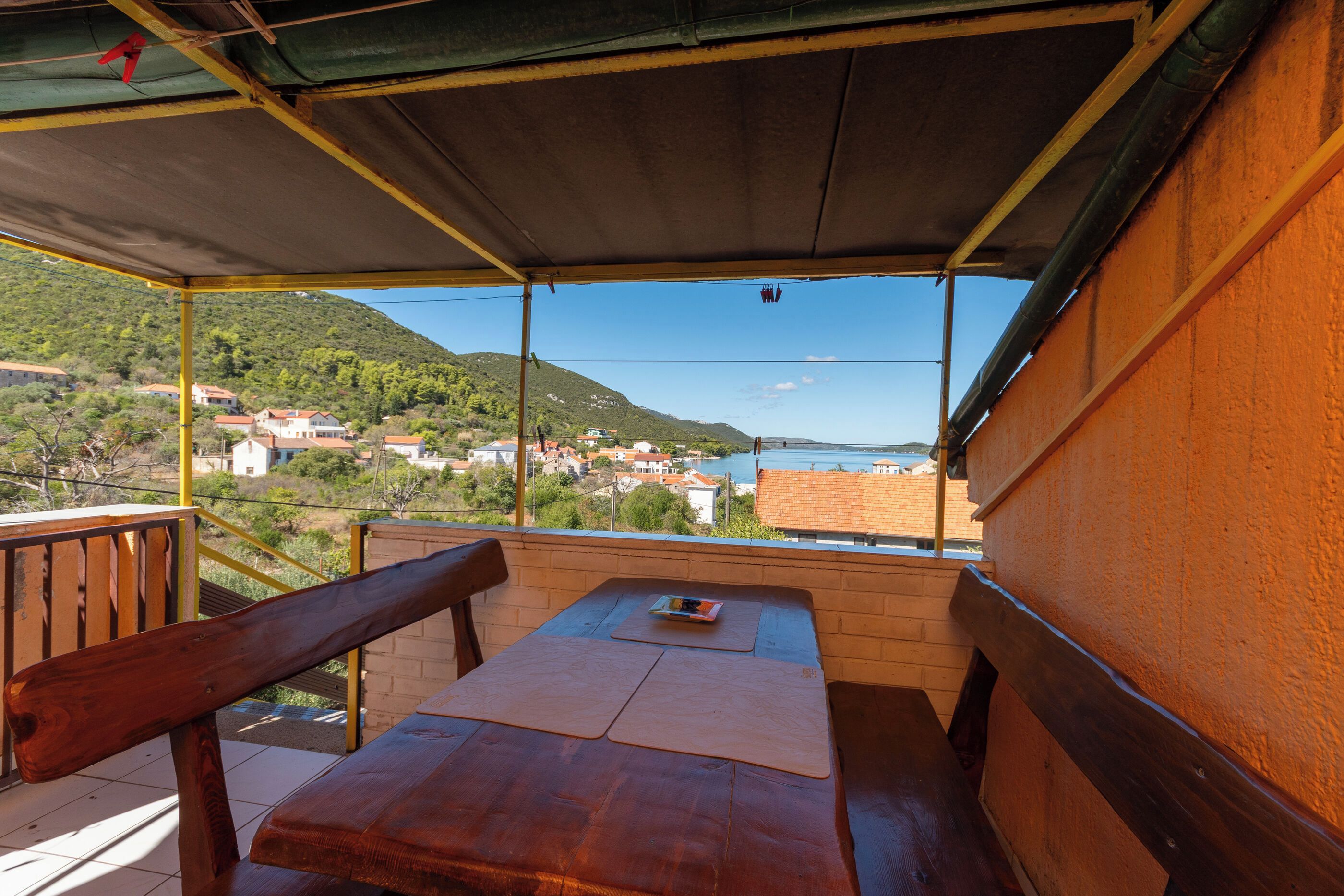 A wooden bench and table under a shaded area with a view of a hillside and a body of water.