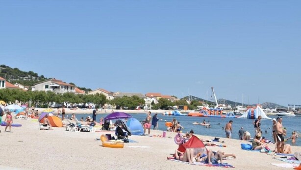 A beach with people sunbathing, swimming, and playing. There are umbrellas, beach chairs, and a few tents. - Apartment Antonio (Murter-Kornati)