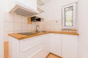 A kitchen with white cabinets, a wooden countertop, a sink, and a window with blinds. - Apartments Mir (Dugi Rat)