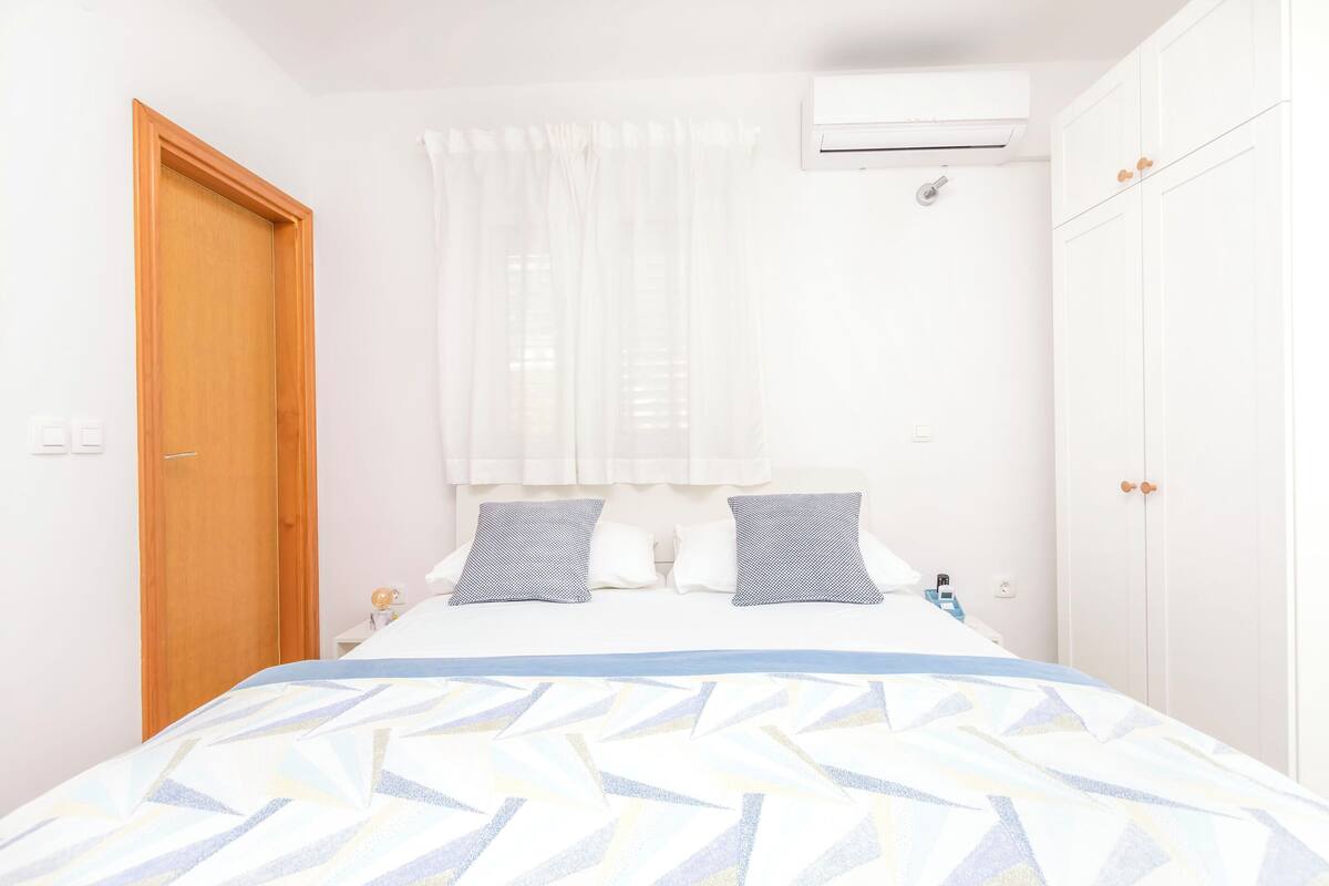 Une chambre à coucher avec un lit, une porte en bois, une armoire blanche et une fenêtre ornée de rideaux légers.
