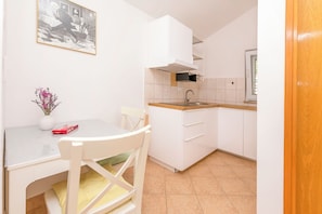 Cocina compacta con muebles blancos, encimera de madera, un lavabo y una zona de comedor con una silla y una mesa.