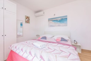 Un dormitorio con una cama, una mesita de noche, aire acondicionado y un cuadro en la pared.